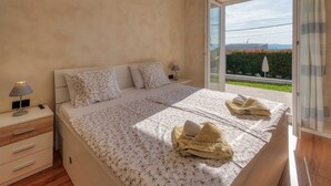 Un dormitorio con cama, mesita de noche, lámpara y vistas a un jardín a través de una puerta corredera.