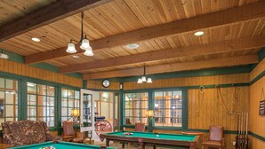 Une salle de billard aux murs en bois, aux boiseries vertes et où l’on trouve plusieurs tables de billard.