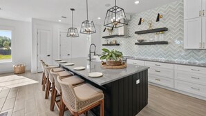 A modern kitchen with a central island, bar stools, pendant lights, and a herringbone-patterned backsplash. - Fall is Near and the Most Wonderful time of year! (Panama City Beach)