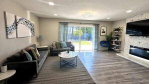 A modern living room with a sofa, coffee table, and TV, featuring a patterned rug and wooden flooring. - *Moonlight Cinema* - 15 min to Legoland! (Vista)
