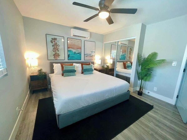 A bedroom with a bed, bedside tables, a ceiling fan, wall art, and a potted plant.