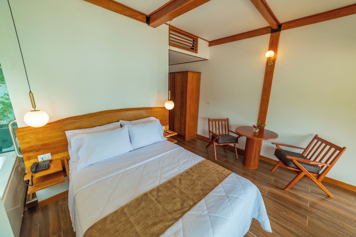 Un dormitorio con una cama grande, cabecera de madera, mesitas de noche, un escritorio, una silla y una pequeña mesa redonda con una planta.