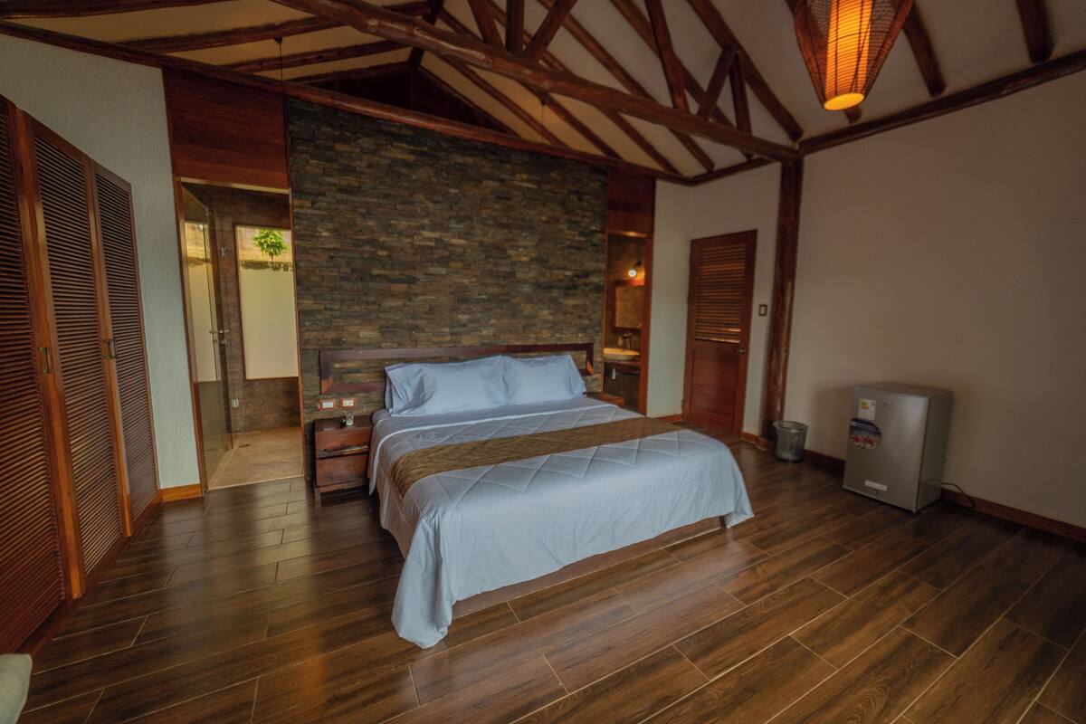 Un dormitorio con una cama grande, vigas de madera, una pared de piedra y un refrigerador.