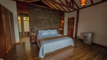 Un dormitorio con una cama grande, vigas de madera, una pared de piedra y un refrigerador.