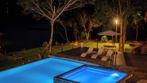 Una piscina con un borde iluminado en azul, rodeada de sillones de descanso y una terraza de madera.