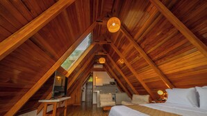 Un dormitorio en el ático con vigas de madera, una cama, un escritorio y una kitchenette.