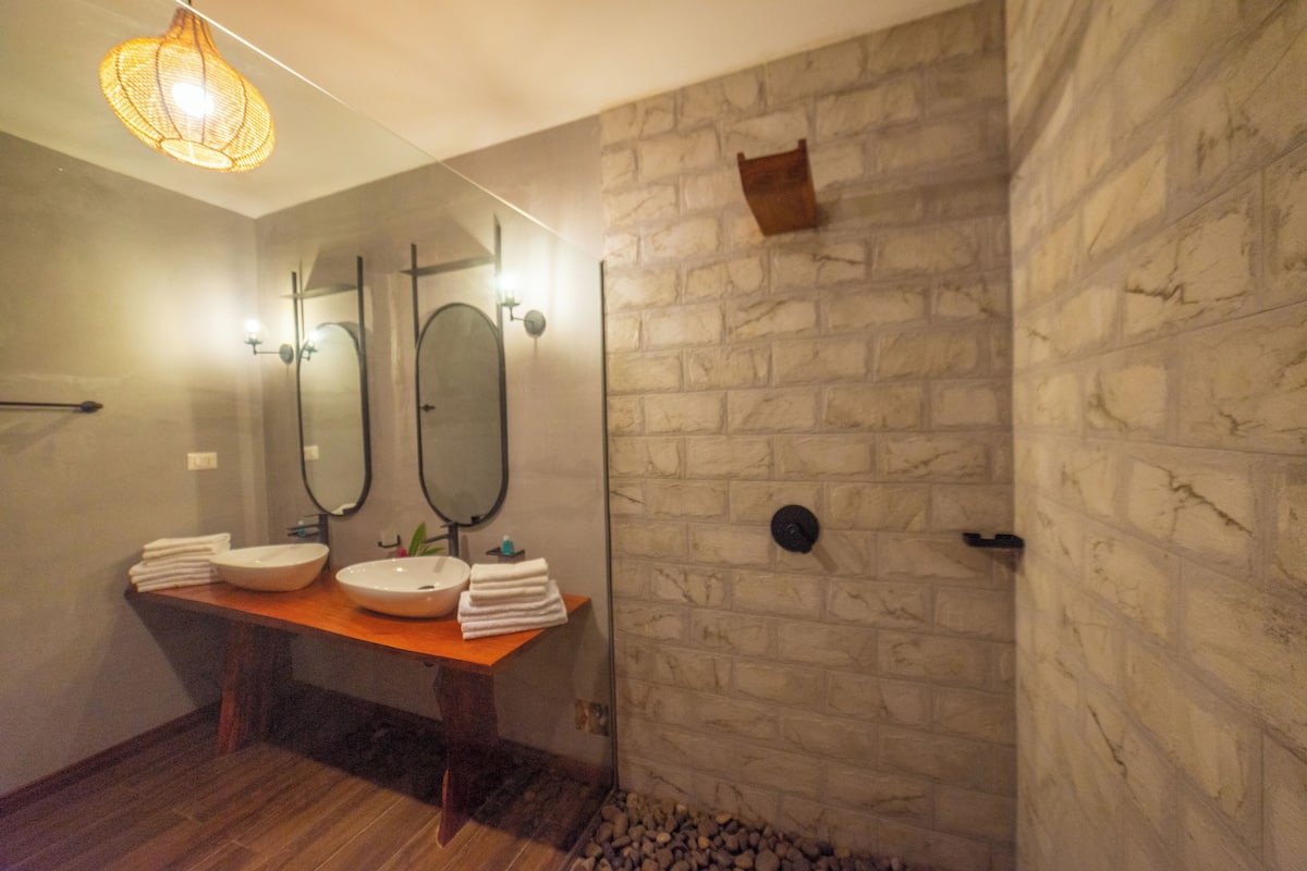 Un baño con tocador de madera, dos lavamanos, un espejo y una pared de piedra.