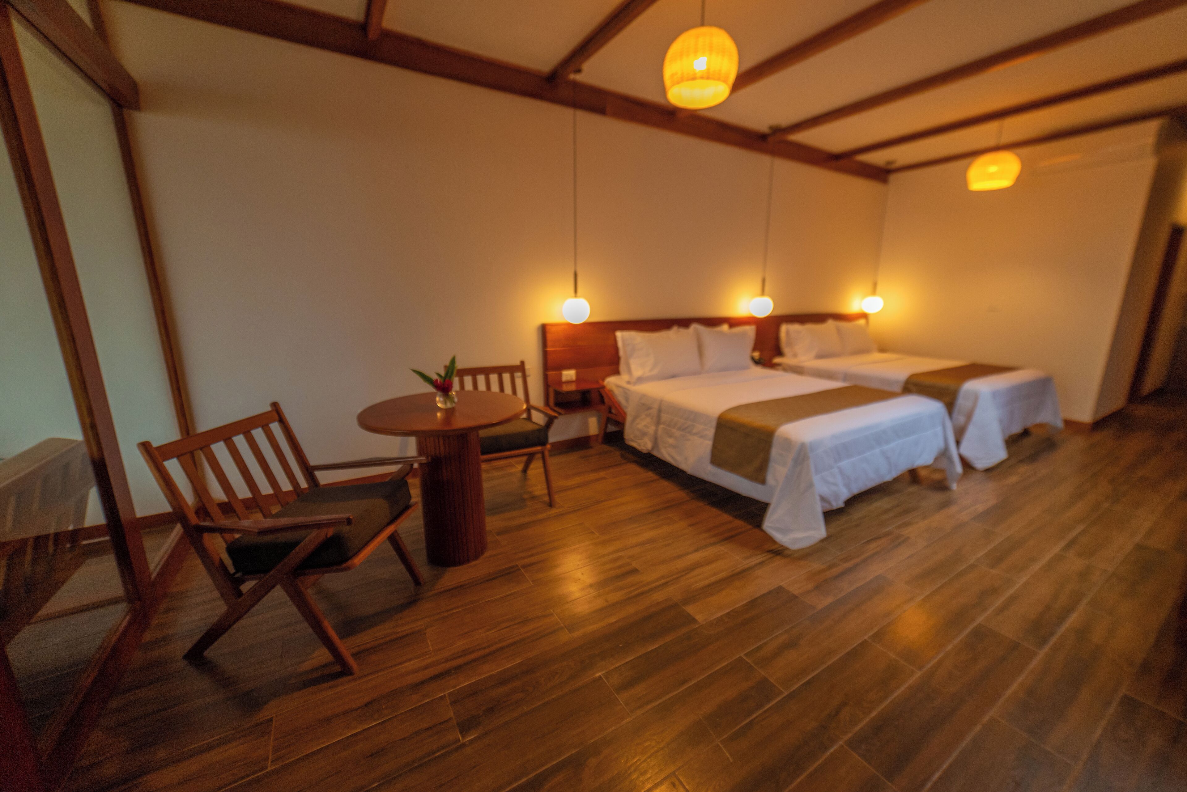 Une chambre avec deux lits, une chaise en bois, une petite table et un luminaire suspendu.