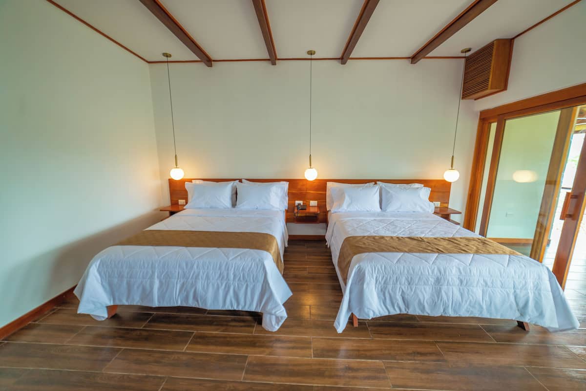 Habitación de hotel con dos camas, piso de madera y un ventanal amplio.