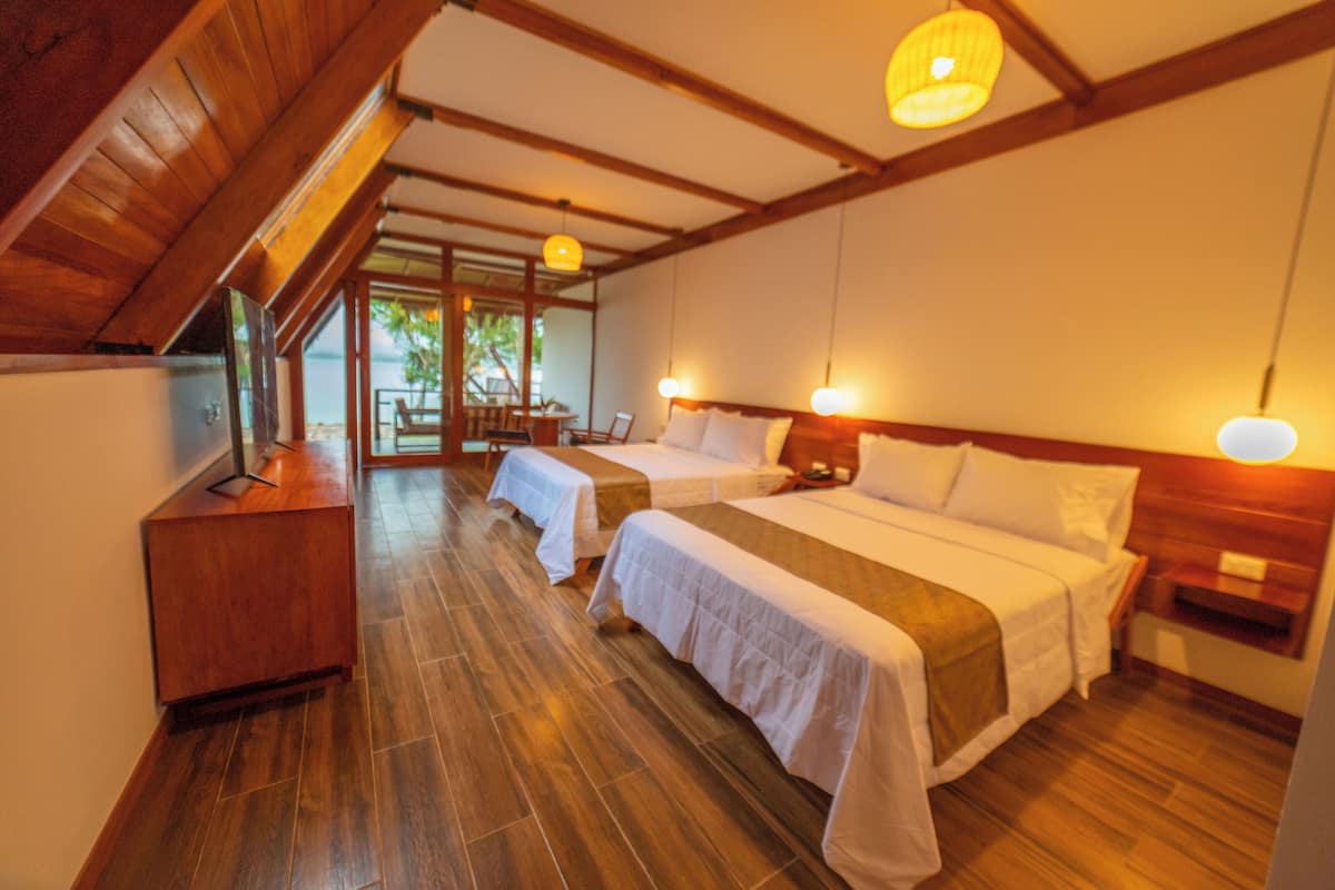 Habitación de hotel con dos camas, suelo de madera, un escritorio y vistas al exterior.