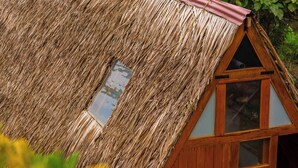 Una construcción con techo de paja, ventana triangular y puerta de madera.