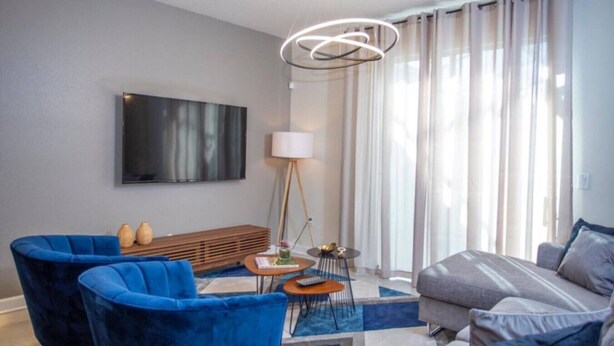 Un salon moderne avec un canapé, un fauteuil bleu, une table basse, un lampadaire et un téléviseur à écran plat fixé au mur.