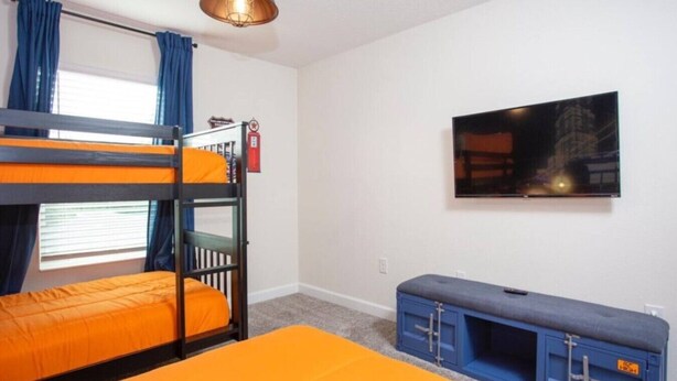 A room with bunk beds, a television, and a bench.