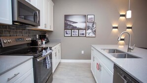 A modern kitchen with a microwave, stove, and dishwasher. There are framed pictures on the wall and pendant lights above the sink.