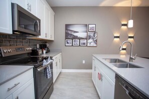 A modern kitchen with a microwave, stove, and dishwasher. There are framed pictures on the wall and pendant lights above the sink.