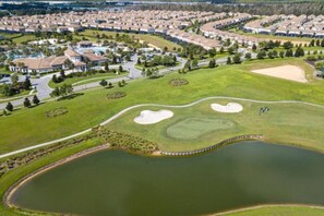 A golf course with bunkers, a pond, and a residential area in the background.