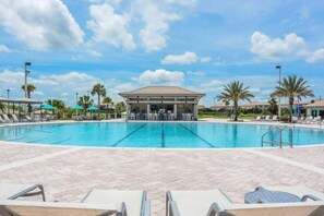 A swimming pool with lounge chairs and umbrellas, a covered seating area, and palm trees.