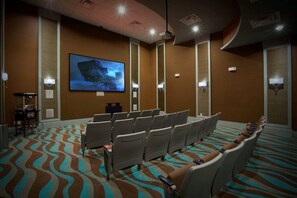 A conference room with rows of chairs, a large screen, and a patterned carpet.