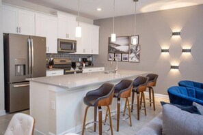 A modern kitchen with a central island, bar stools, and a seating area with a blue sofa. - 4BR ChampionsGate Private Pool Lazy River Access (Davenport)