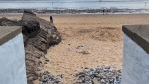 Ein Strand mit einem steinigen Pfad, der zum Ufer führt, feinem Sand und dem Meer im Hintergrund.