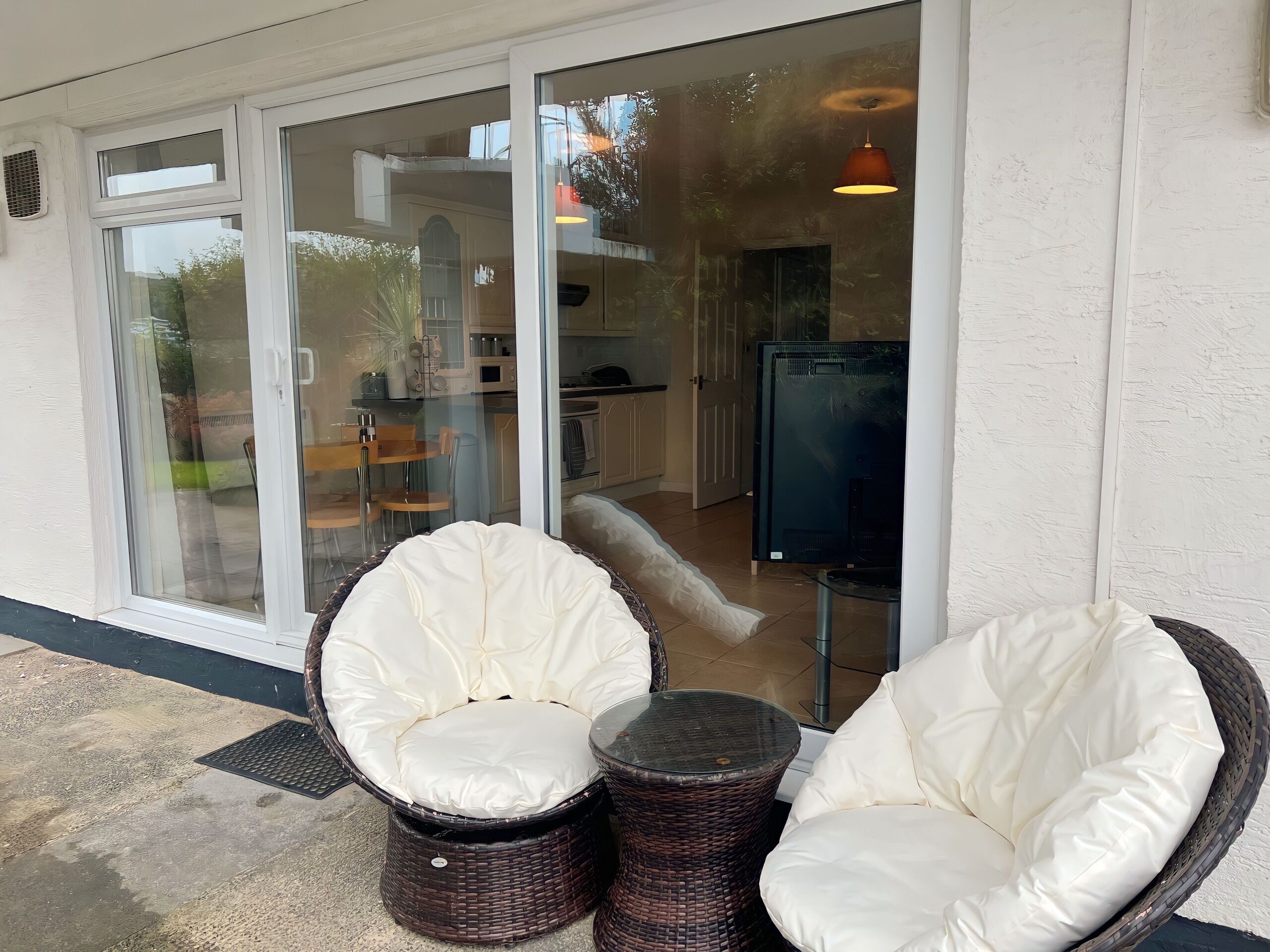 A modern outdoor seating area with wicker chairs and a glass door leading to a kitchen.