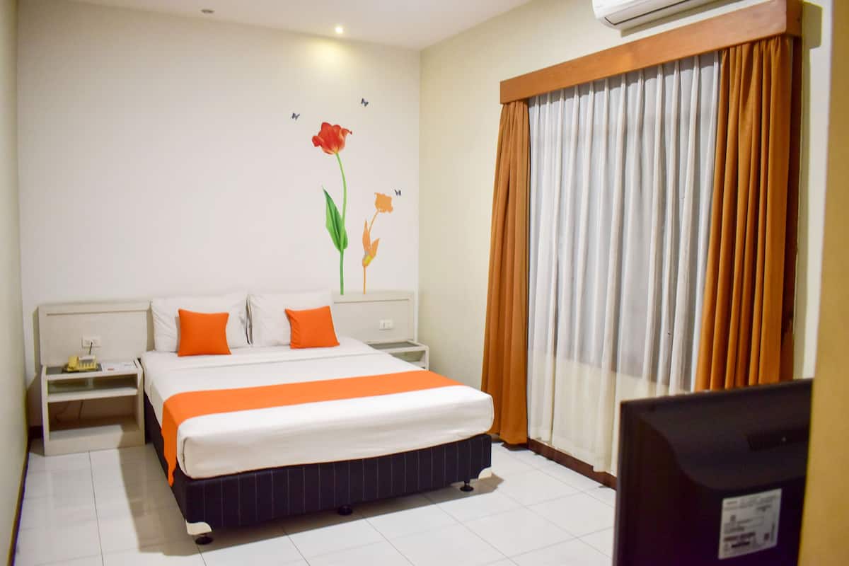 A hotel room with a large bed, white walls, a nightstand, an air conditioner, and a window with curtains.