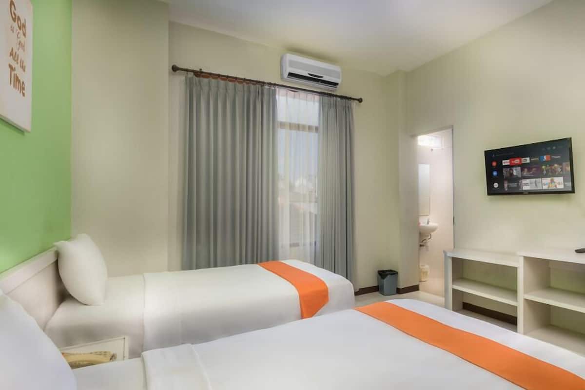 A hotel room with two beds, a TV, a desk, and a window with curtains.