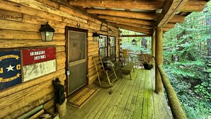 Una baita di legno con veranda, pareti di legno, una porta con un cartello, una panchina e un tavolo.