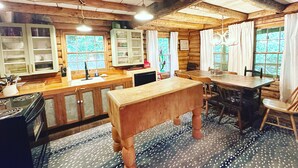 Interno di un rustico chalet con travi in legno, un tavolo da pranzo, sedie, angolo cottura con pensili e pavimento decorato.