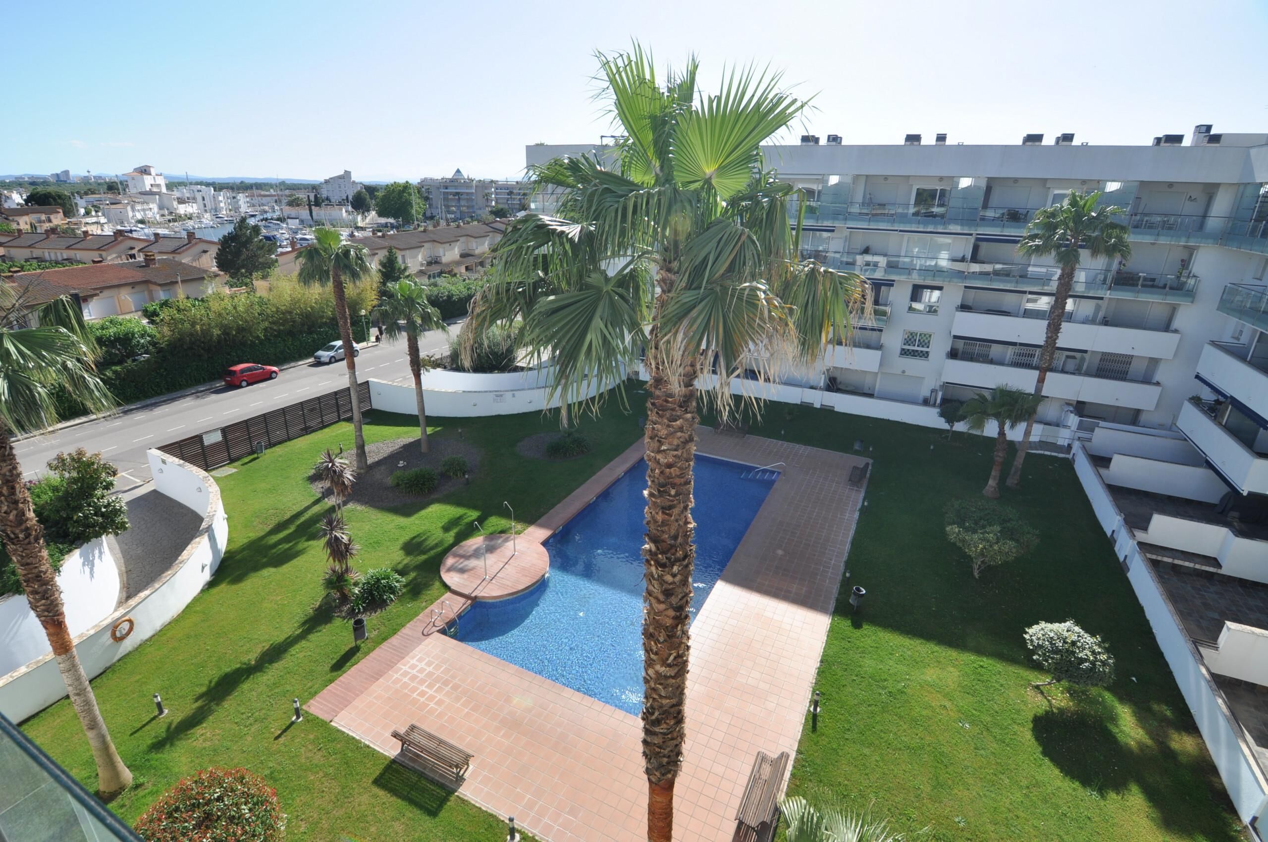 A residential building with a swimming pool surrounded by palm trees and a well-maintained lawn.