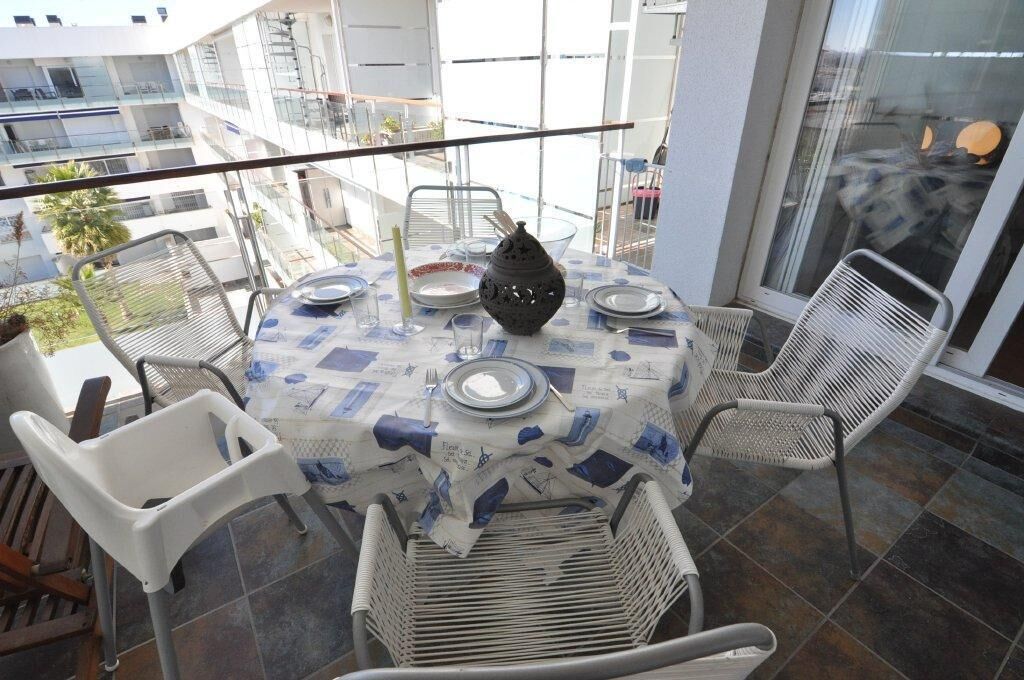 A balcony with a round table set for dining, surrounded by white chairs.