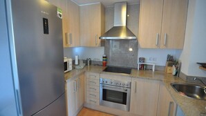 A compact kitchen with a built-in oven, a stainless steel range hood, and wooden cabinets. - Beautiful vacation apartment in Roses, Costa Brava. Bright, modern, sleeps 4 people. Well-equipped and well-located. (Roses)