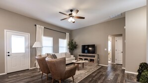 A living room with a sofa, two armchairs, a coffee table, a TV, and a ceiling fan.