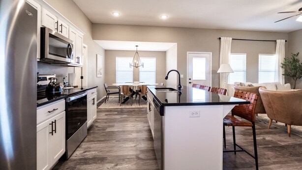A modern kitchen with stainless steel appliances, a dining area with a chandelier, and a cozy seating area with leather chairs.