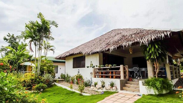 Une maison avec un toit de chaume, un jardin bien entretenu et un chemin pavé menant à l’entrée.