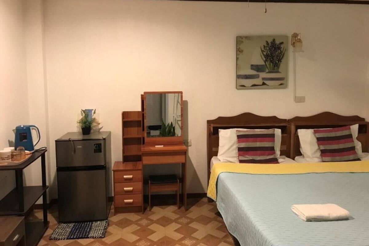 Ein Schlafzimmer mit einem Bett, einem Schreibtisch, einem Kühlschrank, einem Spiegel und einem Deckenventilator.