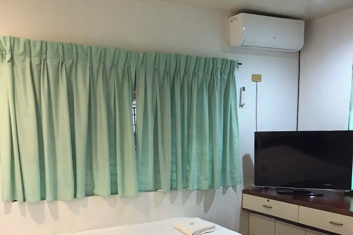 Ein Hotelzimmer mit Bett, Fernseher und einem Vorhangfenster.