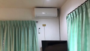 Une chambre dotée d’un téléviseur à écran plat posé sur un meuble en bois, d’un climatiseur fixé au mur et d’une prise de courant.