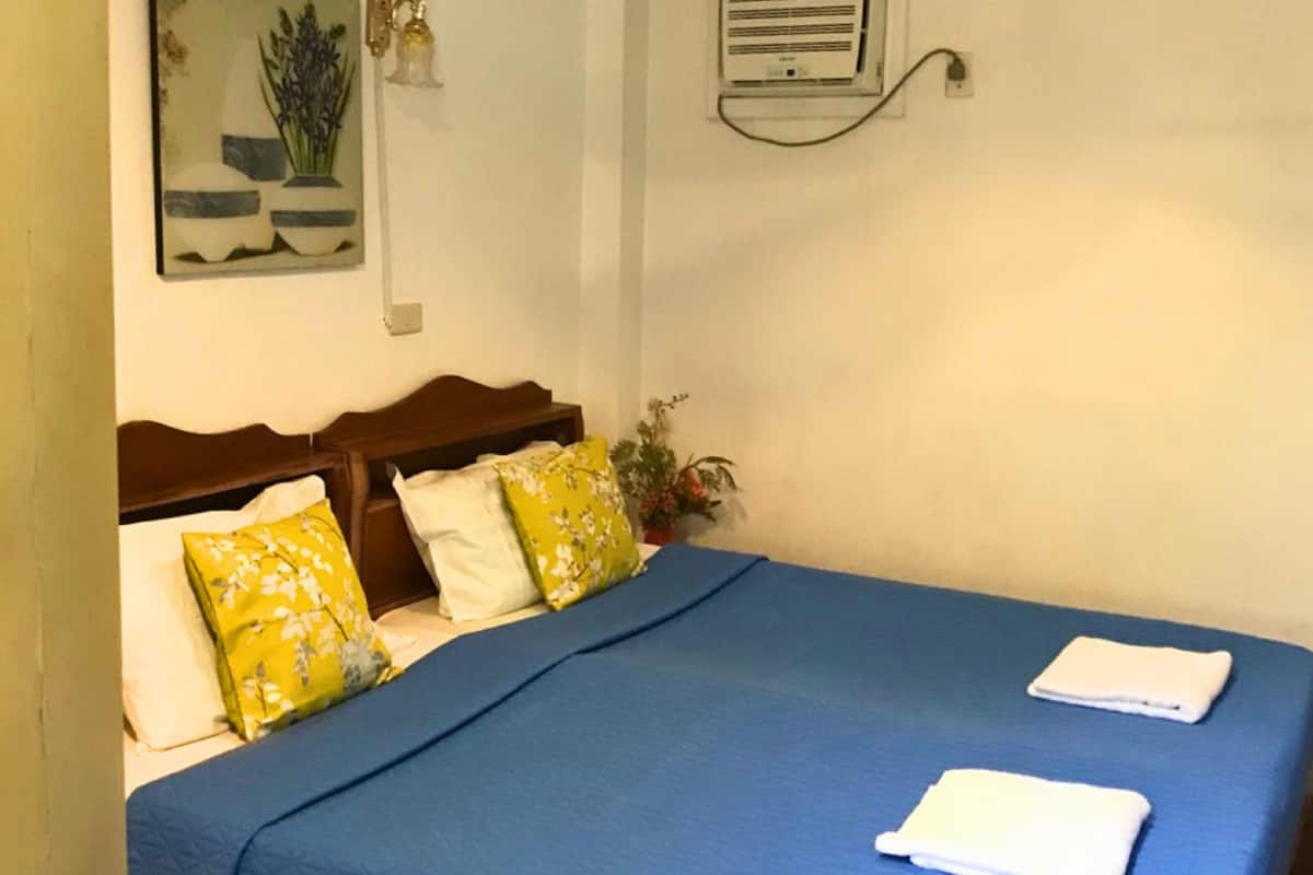 Ein Schlafzimmer mit einer blau gesteppten Bettdecke, zwei Kissen mit Blumenmuster und einem Holzkopfende.
