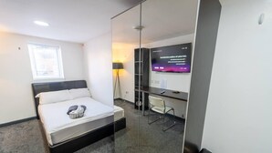 Habitació d'hotel moderna amb un llit, una escriptori, una cadira, una televisió i una separació de vidre.