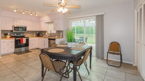 A modern kitchen with white cabinets, a microwave, and a stove. There is a dining table with chairs and a ceiling fan.
