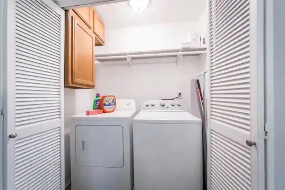 Une buanderie équipée de deux machines à laver, d’un sèche-linge et d’armoires en bois.