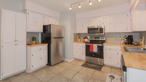 A modern kitchen with white cabinets, stainless steel appliances, and a wooden countertop.