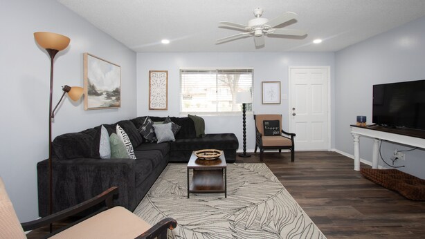 A living room with a dark-colored sofa, a coffee table, a TV, and a ceiling fan.