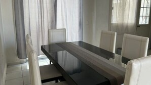 A dining area with a glass-top table and four white chairs. - Relaxing house with pool & self check-in (Mazatlán)