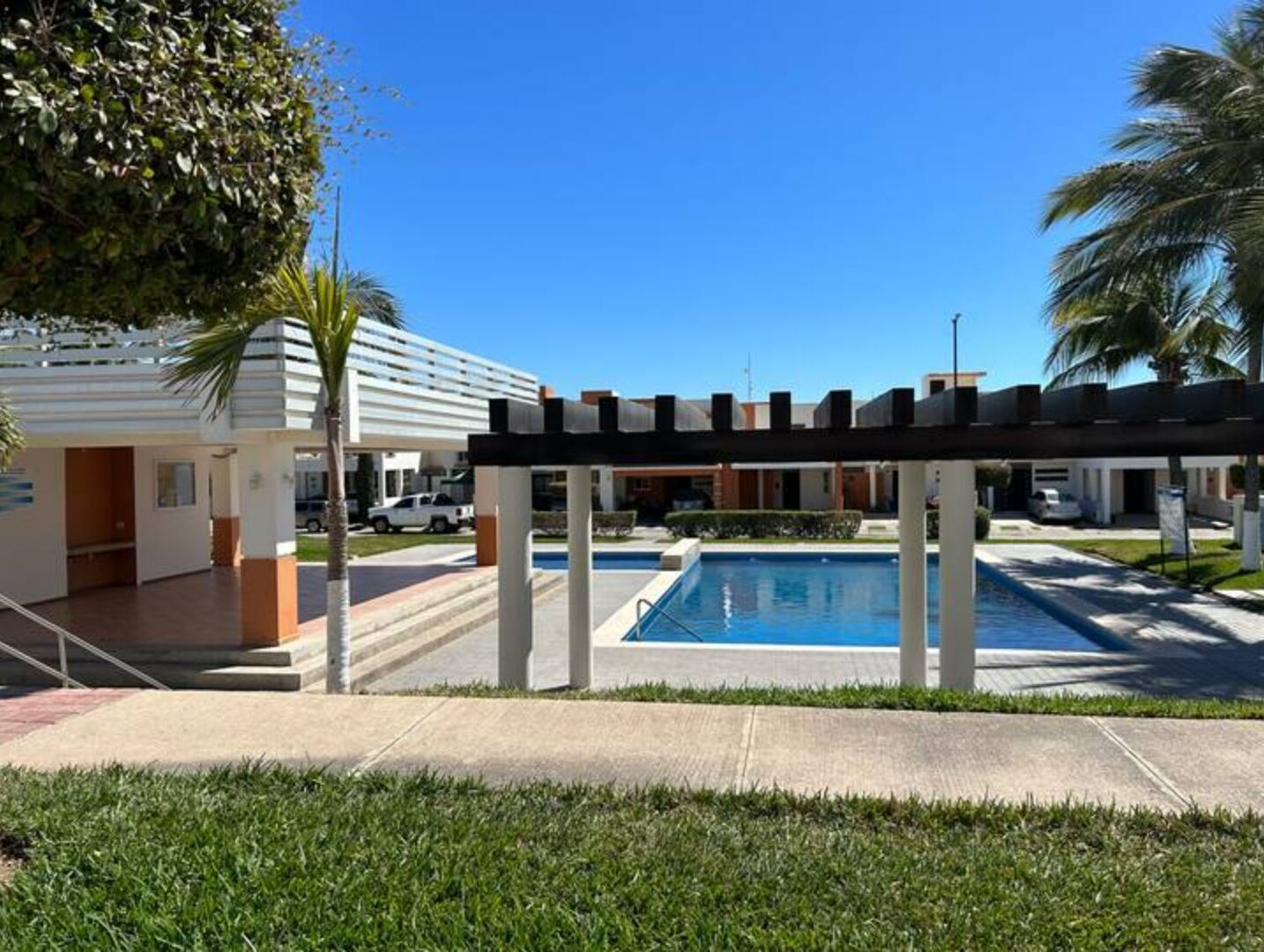 Ein Poolbereich mit einer Pergola, ein Gebäude im modernen Stil und ein klarblauer Himmel.