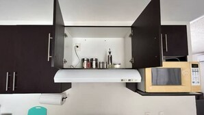 A compact kitchen with dark cabinets, a microwave, a stove, and a small countertop with kitchen items. - Relaxing house with pool & self check-in (Mazatlán)