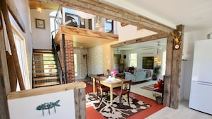 A spacious living area with a dining table, chairs, and a red carpet. A wooden staircase leads to an upper level.