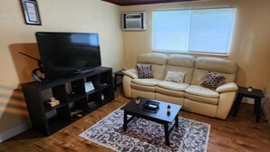 Een woonkamer met een beige bank, een flatscreen televisie, een bijzettafeltje en een kamerkleed met patroon.