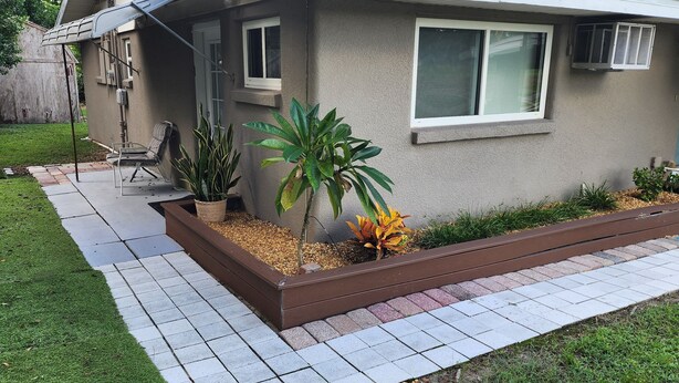 Een woonhuis met een terras, een kleine tuin met planten en een stoel.